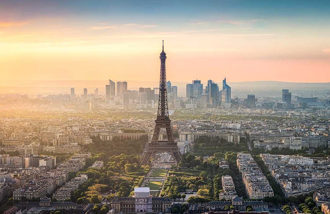 The Eiffel Tower stands tall over Paris with golden sunset hues.