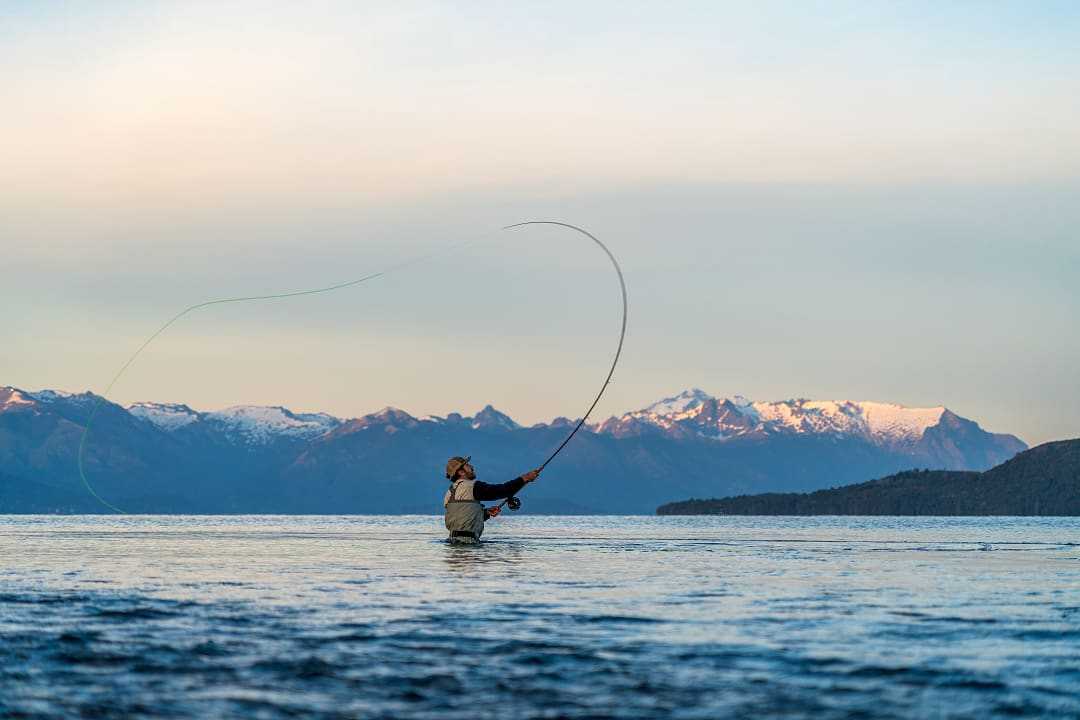 A fisherman casts gracefully in Río Negro’s waters, mountains towering behind.