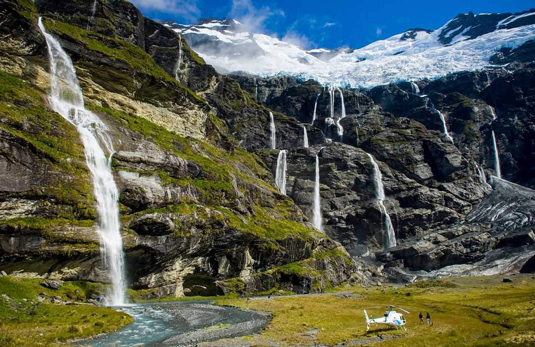 Couple heli hiking at Earnslaw Burn with hanging glacier and cascading waterfalls 