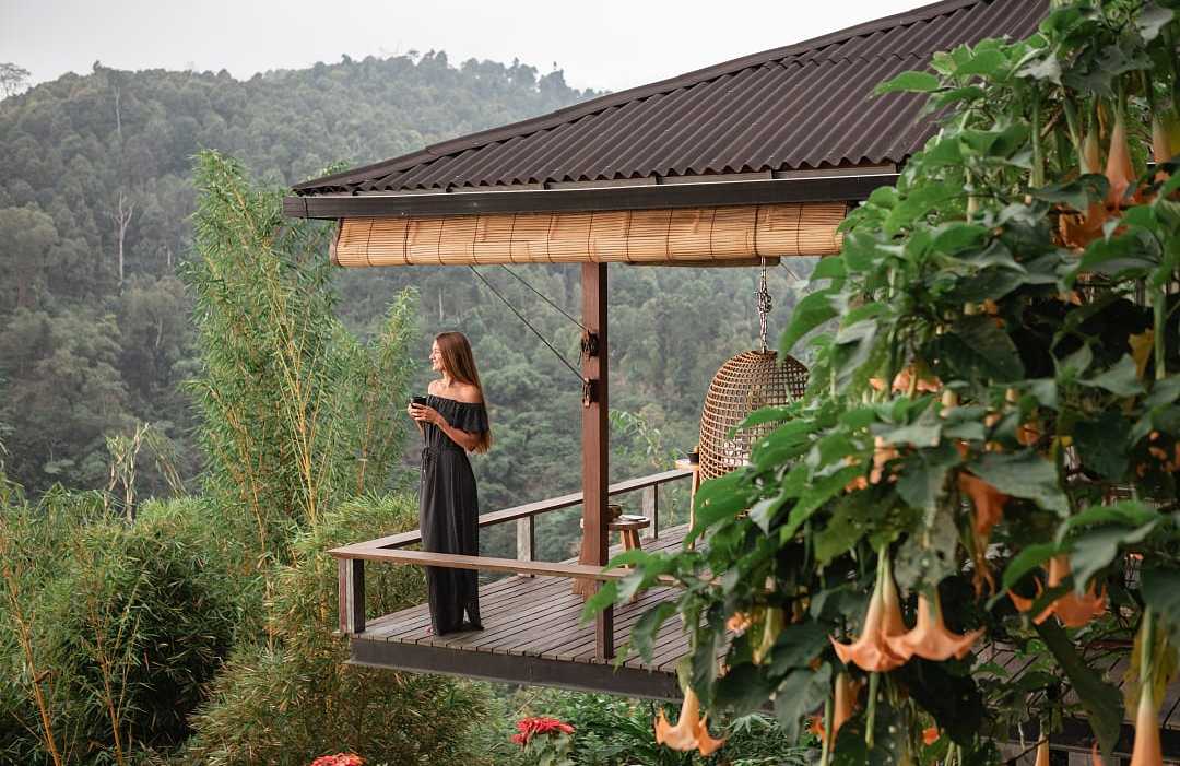 Woman in black dress enjoys coffee on tropical villa balcony.
