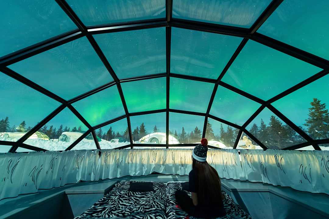 Teen girl watching the Northern Lights from glass igloo in Lapland, Finland