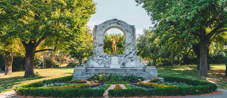 Golden Johann Strauss statue in Stadtpark, Vienna, surrounded by trees and a beautiful garden setting