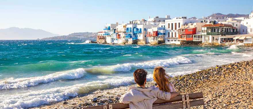 Romantic couple sitting on a beach bench near Little Venice in Mykonos, Greece