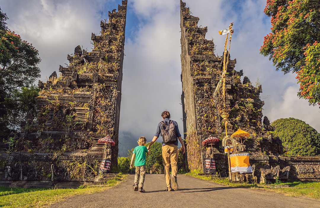 Father and son walking through traditional balinese gate Candi Bentar in Bali, Indonesia