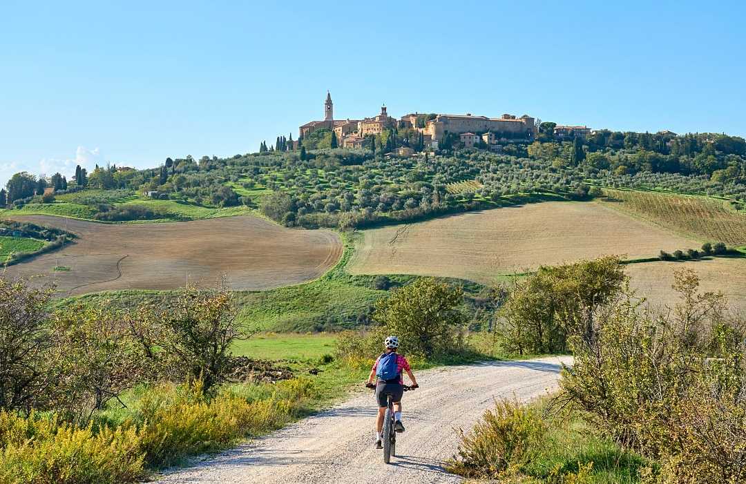Woman biking on dirt road towards Pienza in Tuscany, Italy
