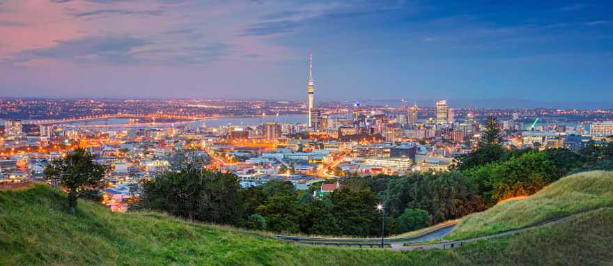 Auckland cityscape at dusk viewed from Mount Eden grassy slopes.