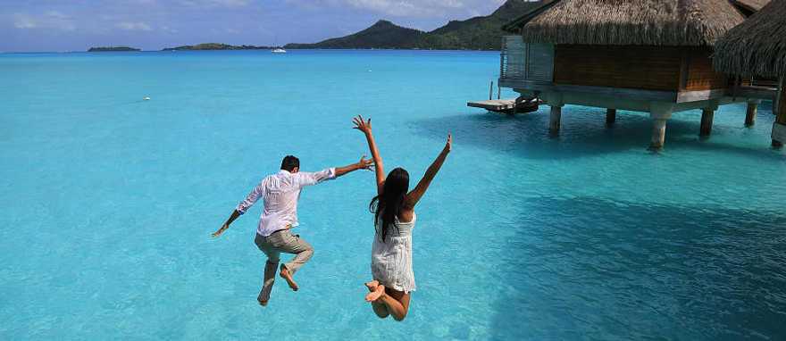 Happy young couple jump into the water from their over water bungalow in Bora Bora