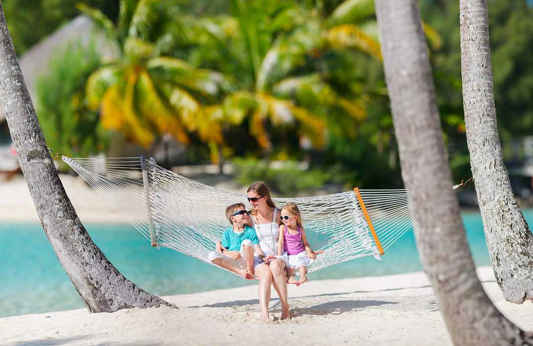 Mother swinging in a hammock on the beach with her kids in French Polynesia