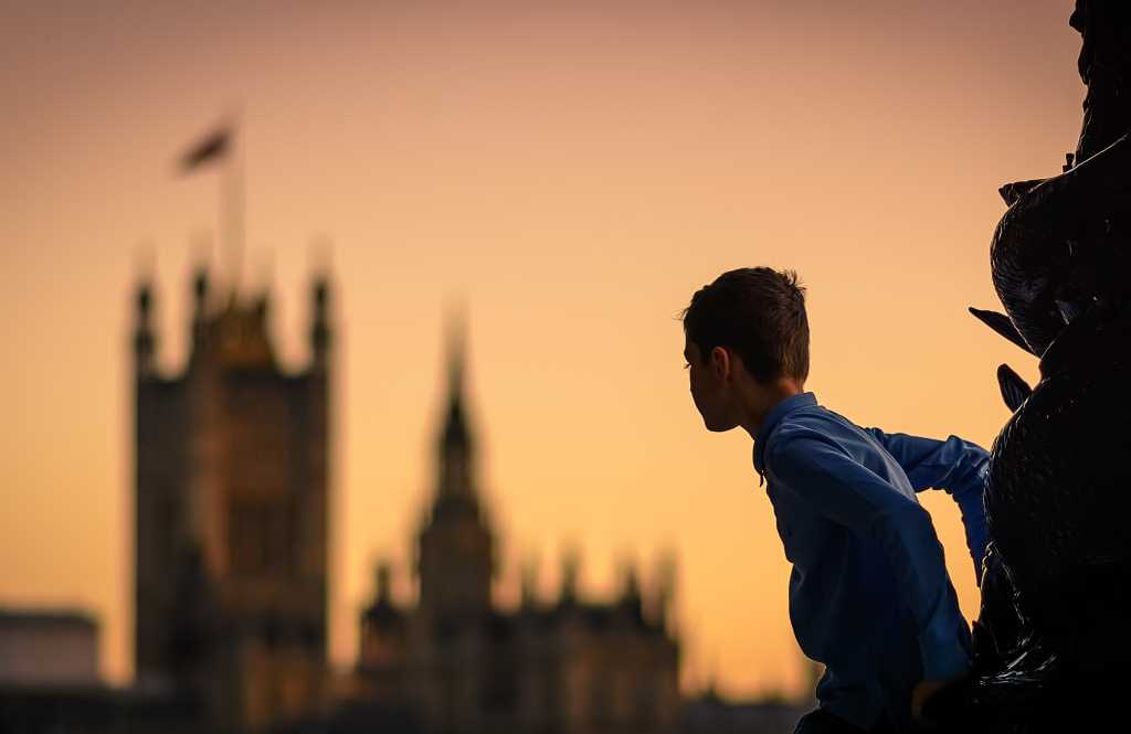Child climbing a lamp post in south bank in london (uk) at sunset with the houses of parliament in the background