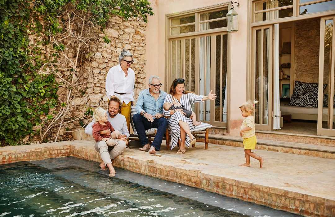 Essaouira, Morocco Smiling grandparents relaxing with children and grandchildren beside pool at villa during multigenerational family vacation
