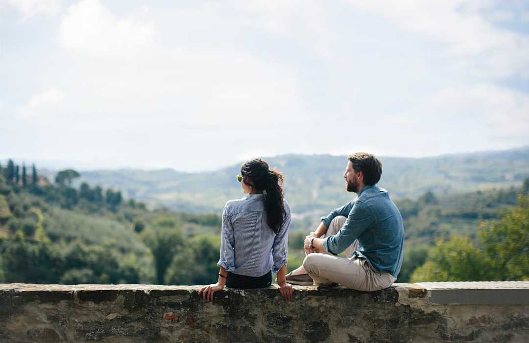 Tuscany, Italy Couple sitting on stone wall overlooking rolling countryside hills in Tuscany, Italy
