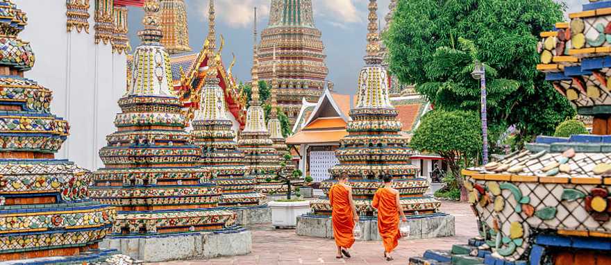 Two monks in colorful orange robes walking through Wat Pho Temple in Bangkok, Thailand