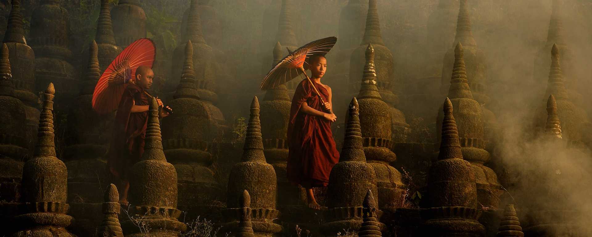 Young novice monks dressed in traditional red robes walk along the ancient stone of Ratanabon Pagoda in Mrauk U, Myanmar